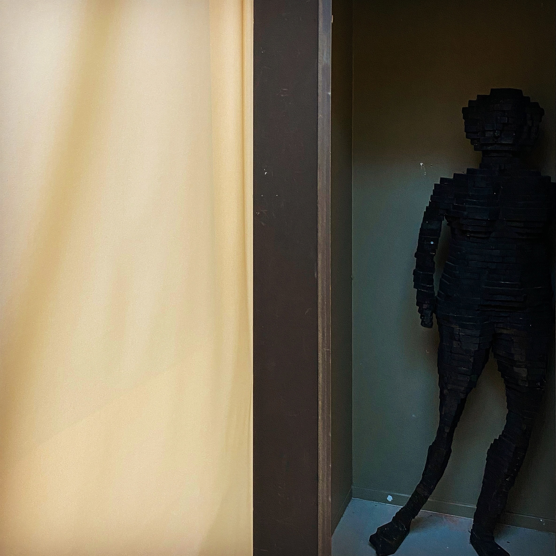 An ominous all-black sculpture with humanoid shape positioned like it is hiding.