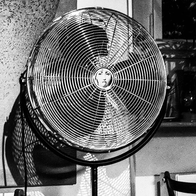 Black and white image of fan with metal cage and picture of a woman's face sticking out her tongue.
