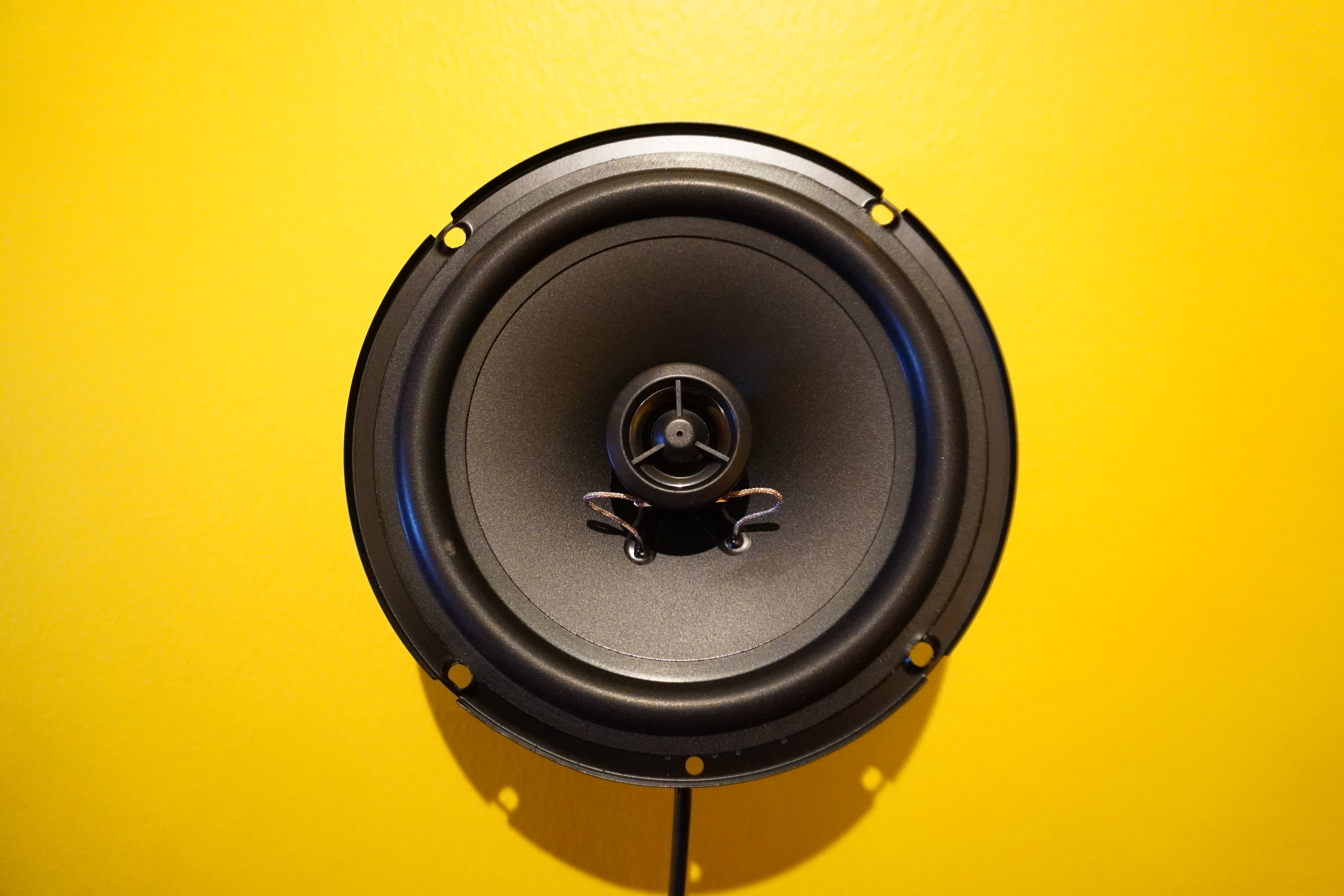 A speaker with cable attached to a bright yellow wall.