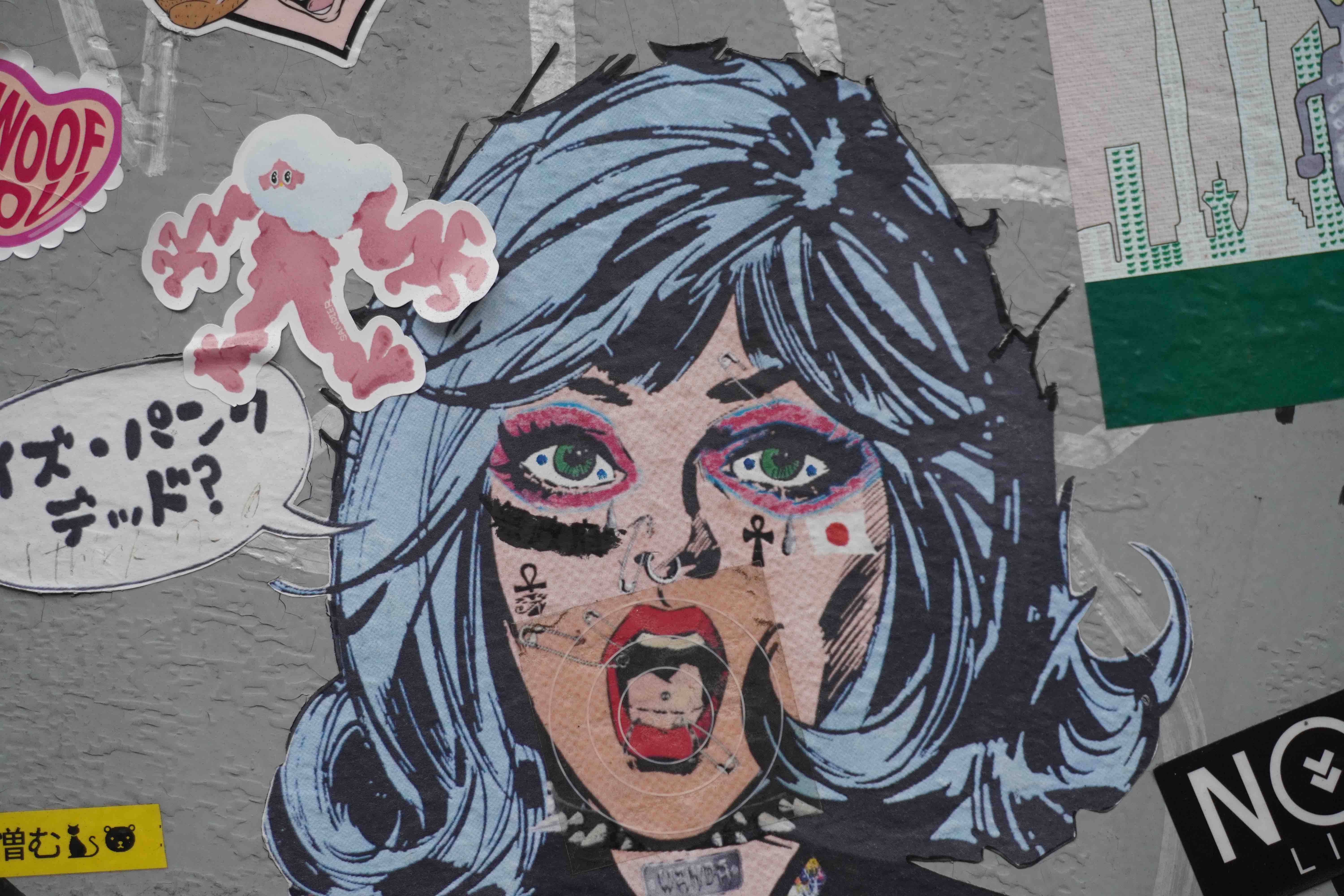 Graffiti and stickers on a wall in Tokyo showing a woman's face in surprise.
