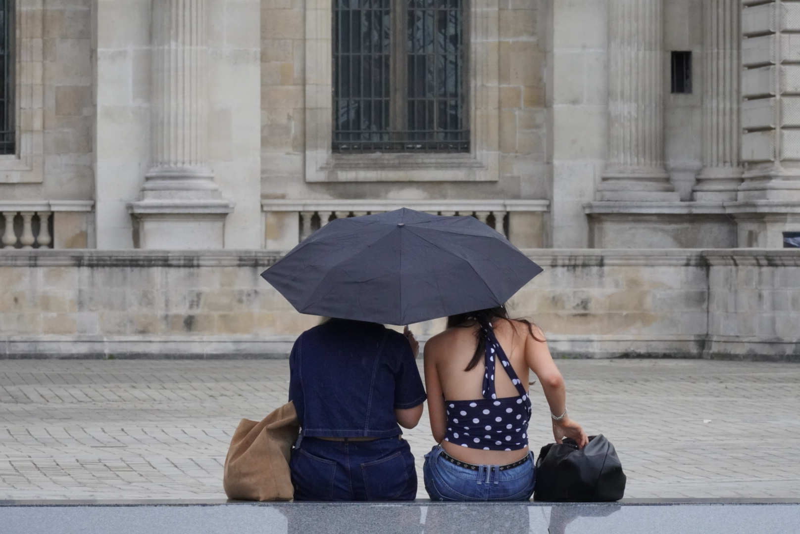 Two women sat at the Louvre in Paris, France facing away from the photographer.